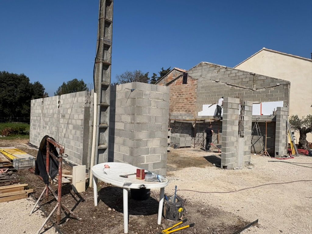 Construction d'un bâtiment aux murs en parpaings de béton, une personne travaille, journée ensoleillée.