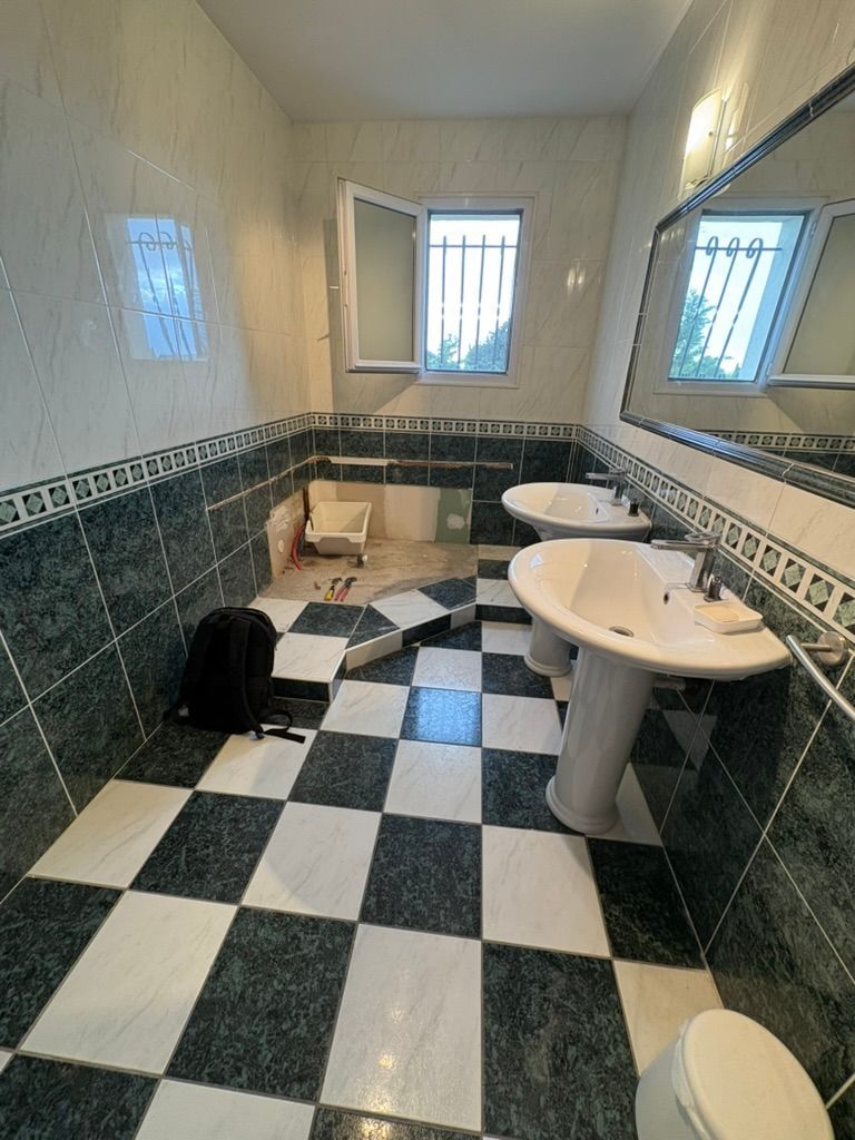 Salle de bains avec murs carrelés verts et blancs et sol à damier, deux lavabos.