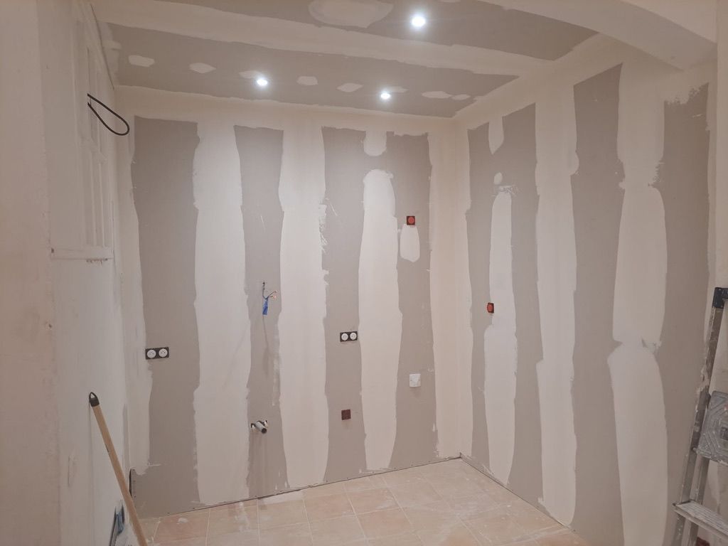 Pièce intérieure avec cloisons sèches, prises électriques, éclairage encastré et échelle ; en construction.