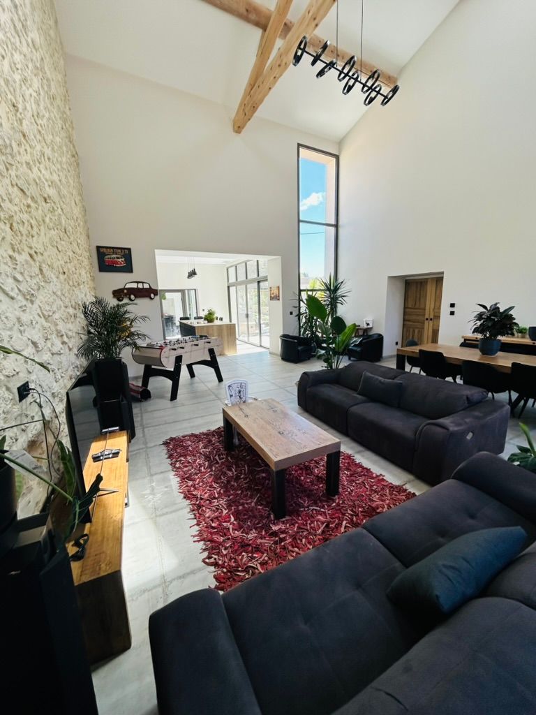 Salon spacieux avec hauts plafonds, poutres apparentes, mur en pierre, canapés foncés et tapis rouge.