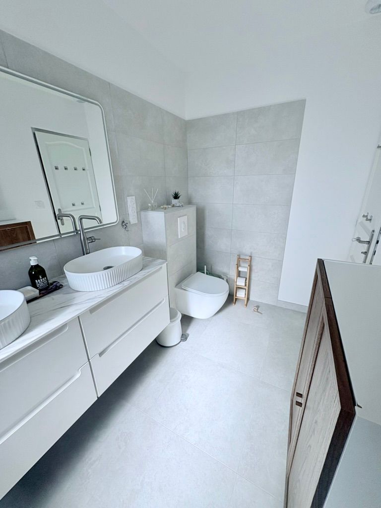 Salle de bains moderne avec meuble-lavabo blanc, toilettes et murs carrelés gris.