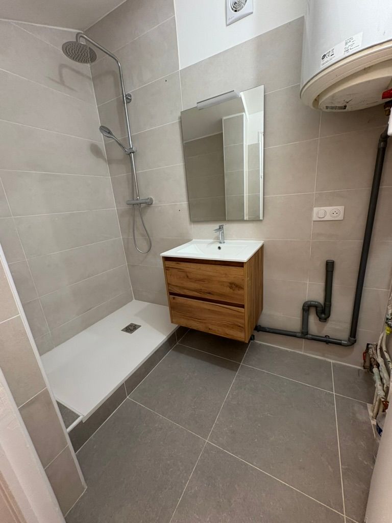 Salle de bains avec carrelage gris, meuble-lavabo en bois, douche et chauffe-eau.