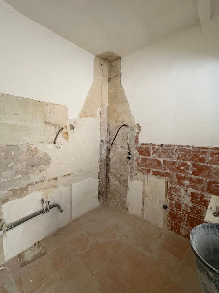 Rénovation de la cuisine en cours : briques apparentes, murs en plâtre, câblage électrique et plomberie visibles.