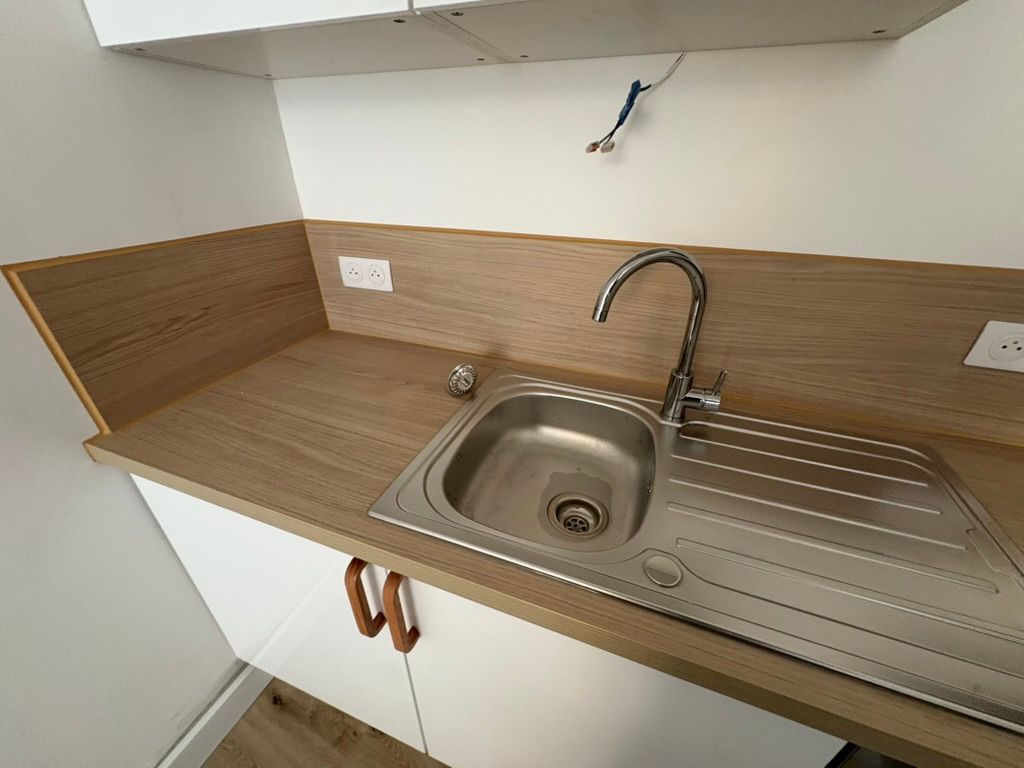 Un évier en acier inoxydable avec un plan de travail imitation bois et des placards blancs.