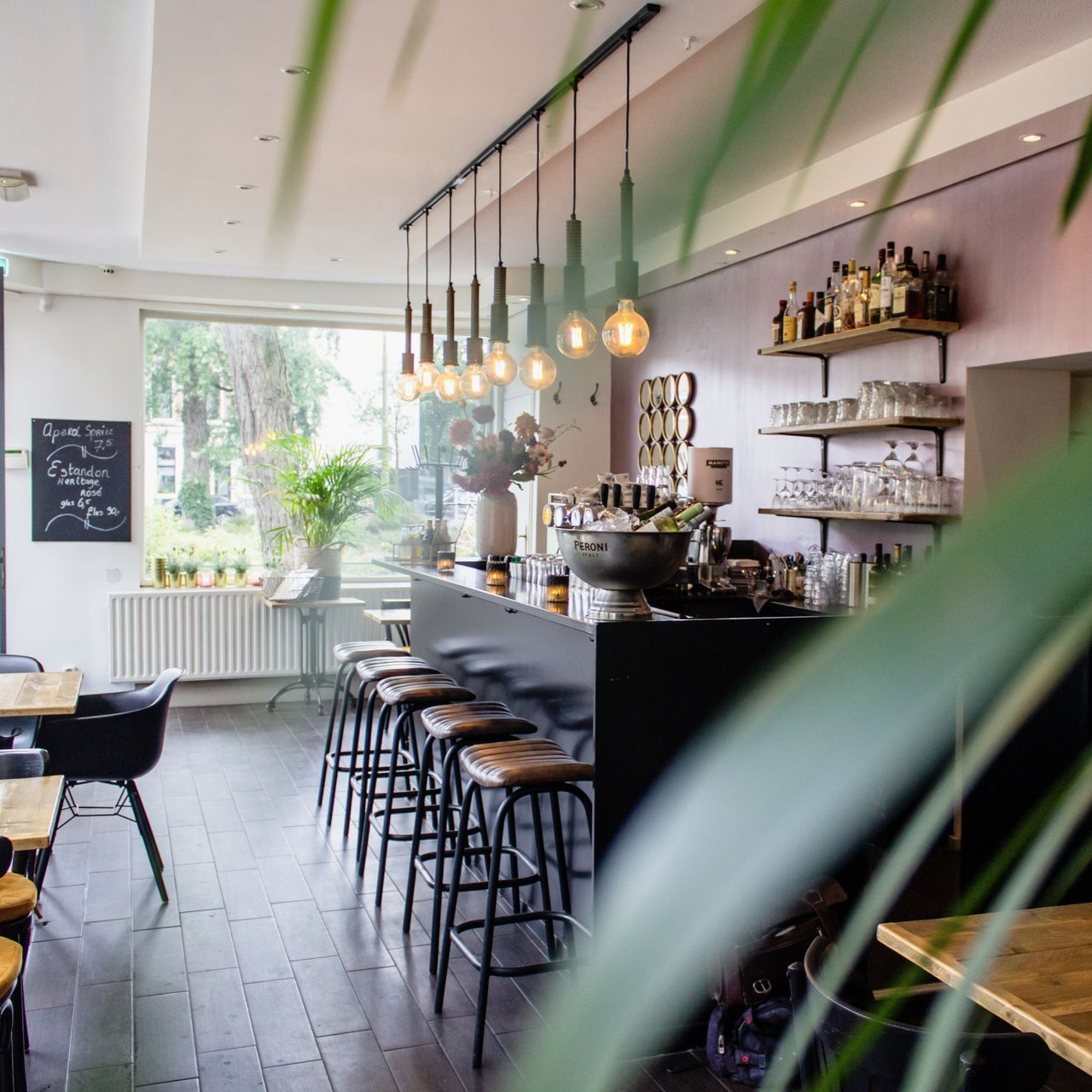 Intérieur d'un restaurant avec bar, tabourets et suspensions lumineuses ; bouteilles sur les étagères, la fenêtre et les tables.