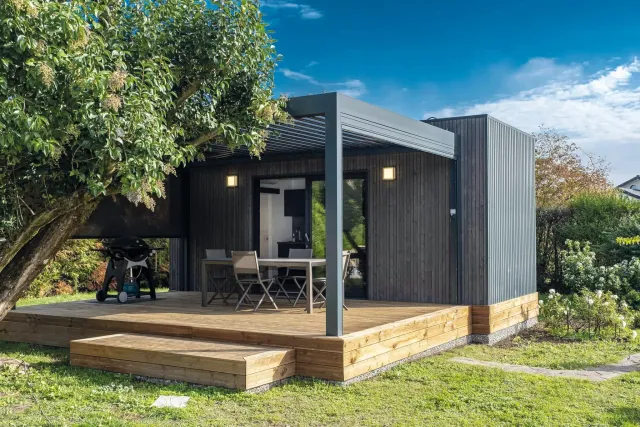 Chalet en bois avec terrasse et mobilier de jardin, sous un ciel bleu.
