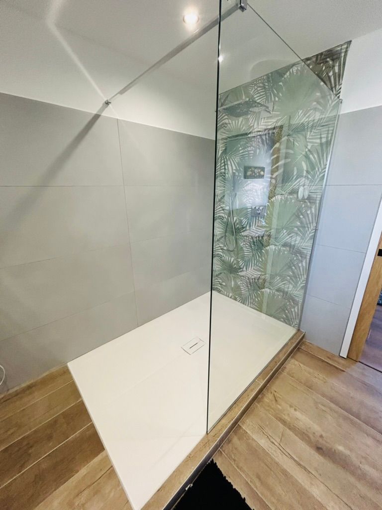 Douche à l'italienne moderne avec parois en verre, receveur blanc et mur carrelé de carreaux verts à motifs.