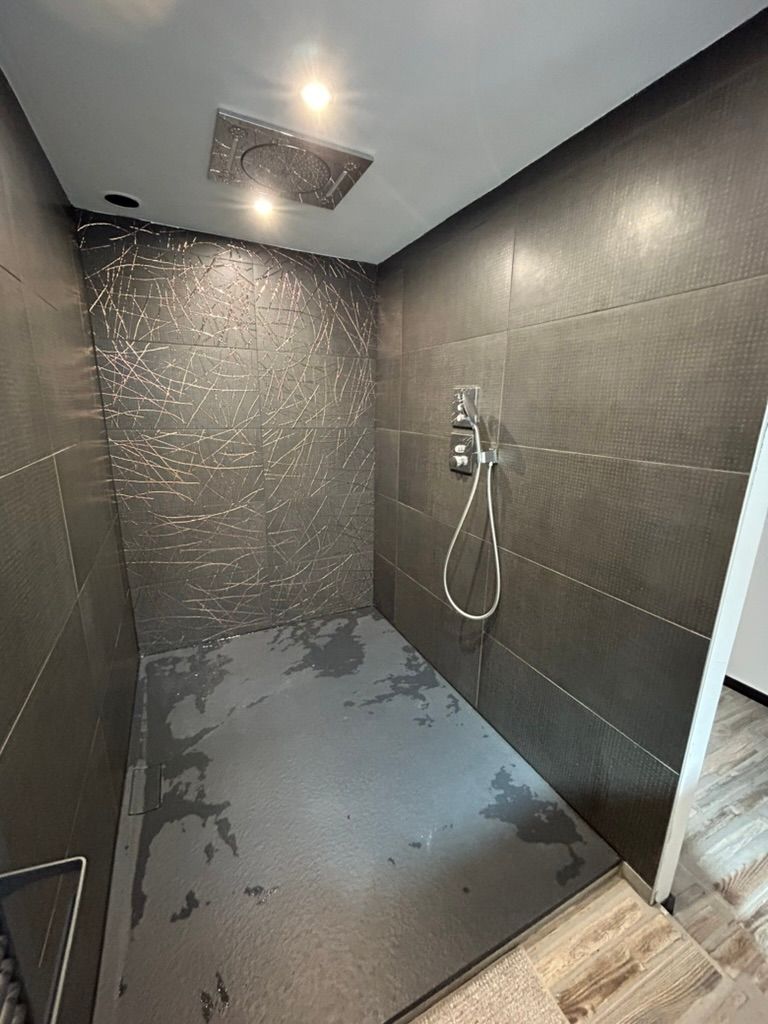 Cabine de douche carrelée gris foncé avec pommeau de douche et douchette.