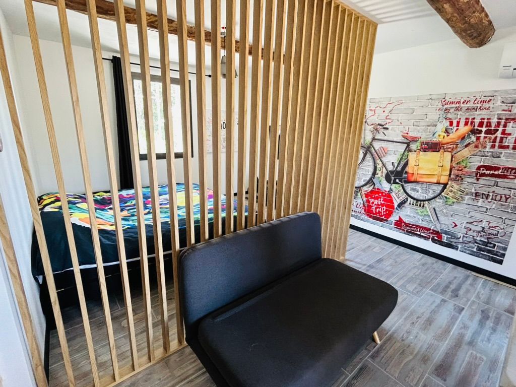 Chambre avec cloison en lattes de bois, petit canapé, lit avec couverture colorée et décoration murale représentant un vélo.