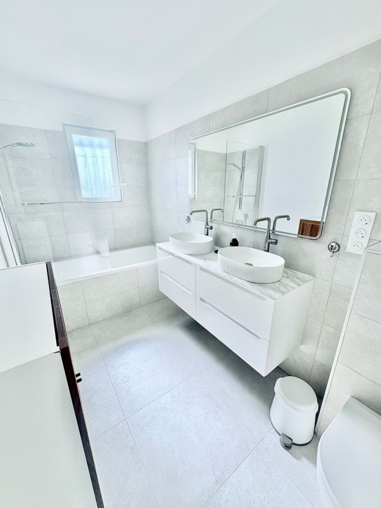 Salle de bains moderne blanche avec meuble-lavabo à double vasque, grand miroir et baignoire.