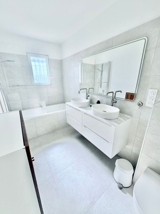 Salle de bains moderne blanche avec meuble-lavabo à double vasque, grand miroir et baignoire.