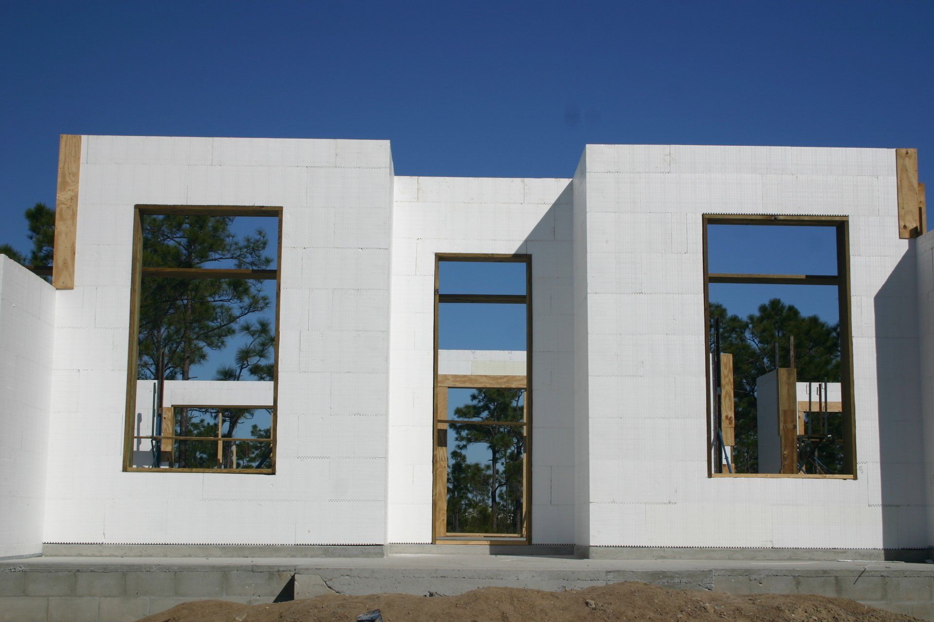 White ICF walls with brown framed windows/door, under clear blue sky, in unfinished construction setting.