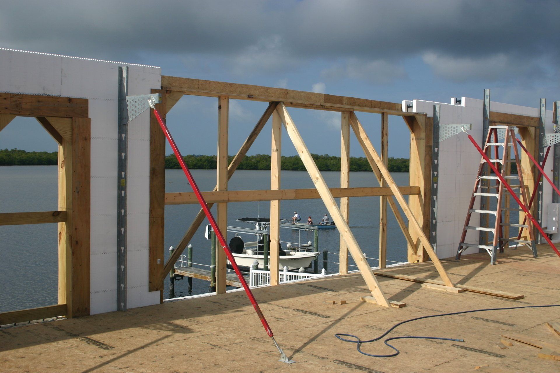 Construction site with wooden frame, bracing, and white blocks, overlooking water.