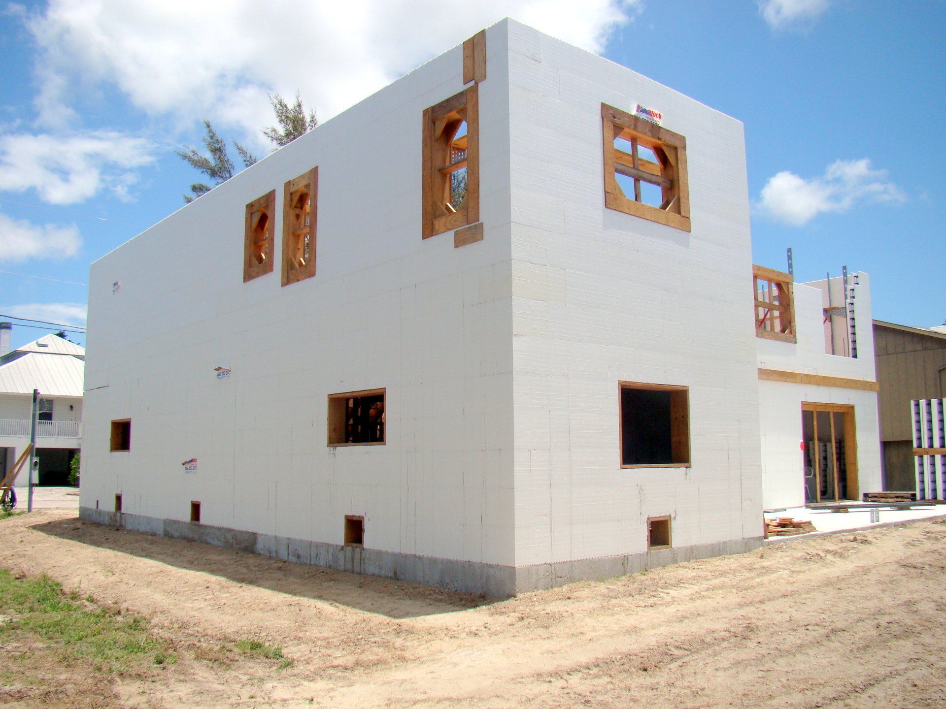 White ICF house under construction; windows framed with wood, sits on a dirt lot under a blue sky.