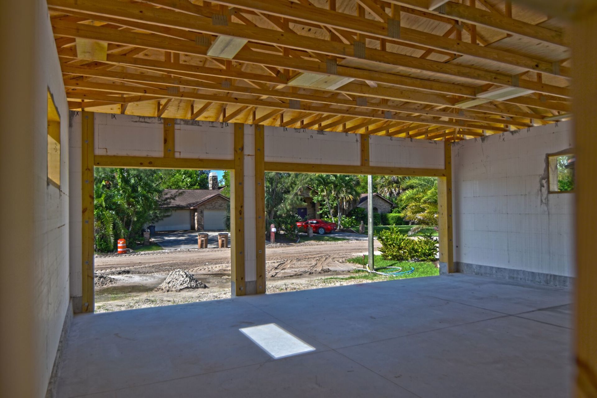 Interior view of a garage under construction, open to the outside with a view of a street and houses.