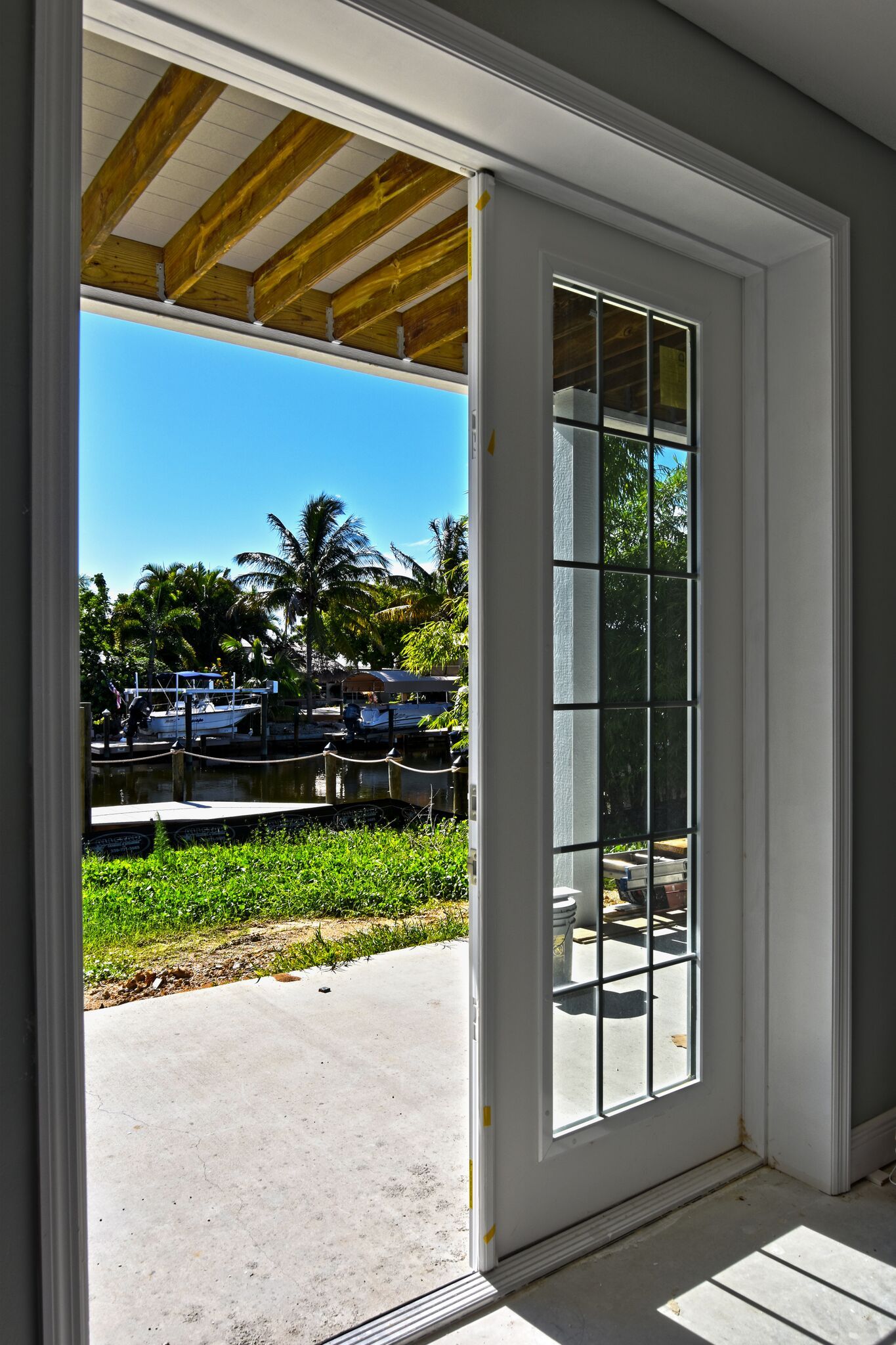 White French door open to reveal a sunny waterfront view with a dock, boats, and blue sky.