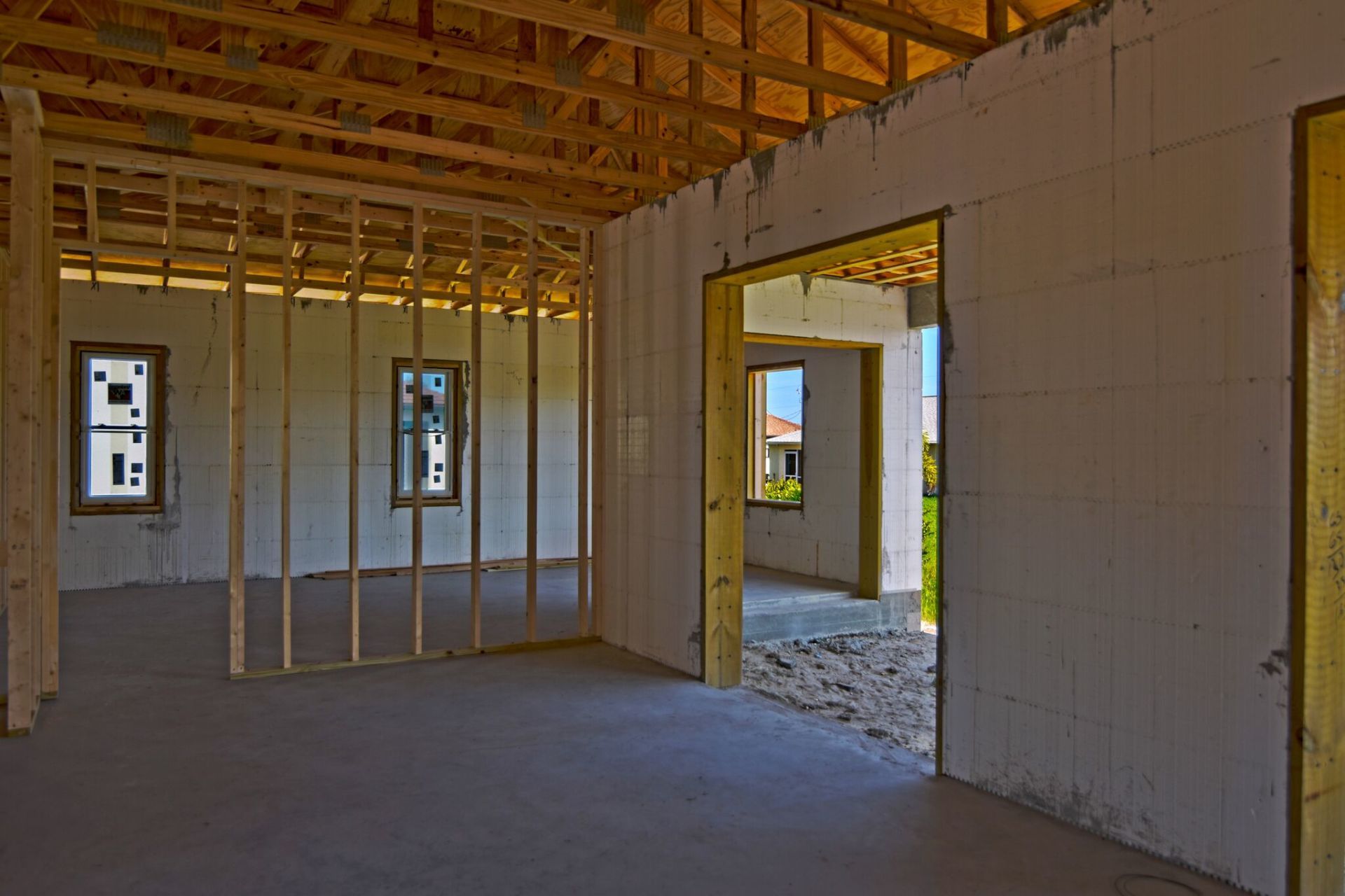 Interior of a house under construction; exposed wood framing, concrete floor, white walls, and open doorways.