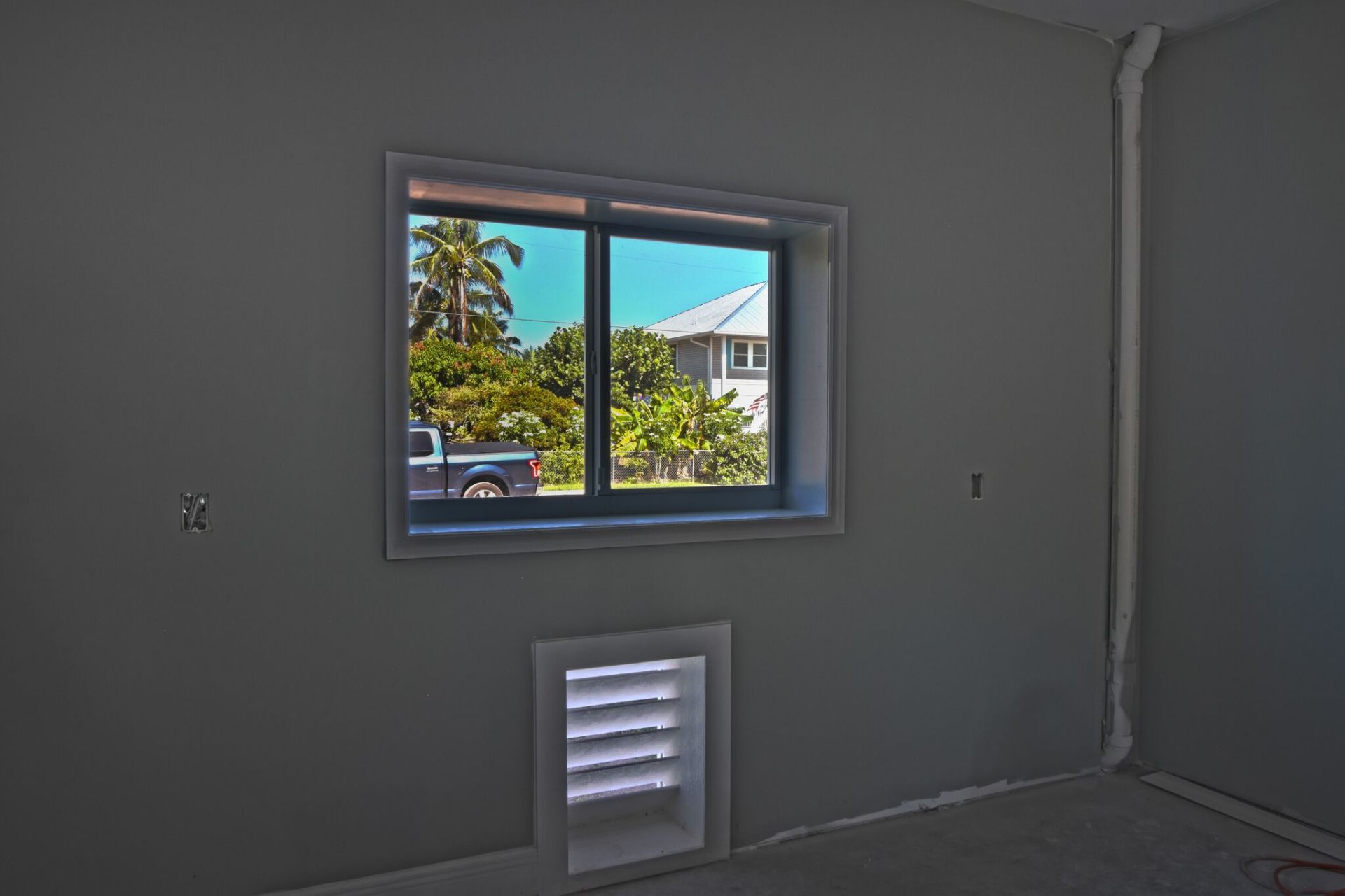 Interior room with a window overlooking greenery and a vent below the window.