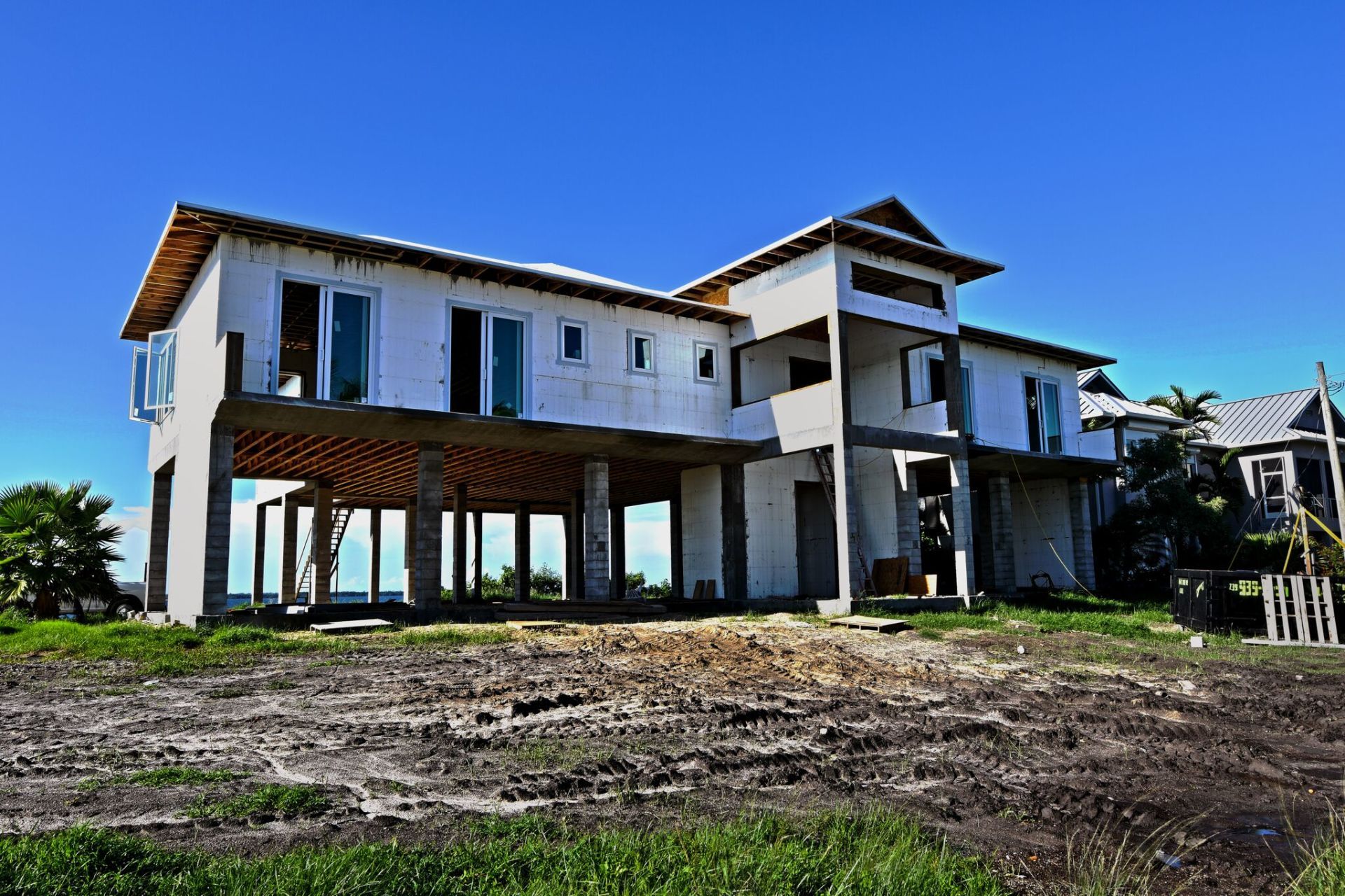 Two-story house under construction on stilts, against a clear blue sky.