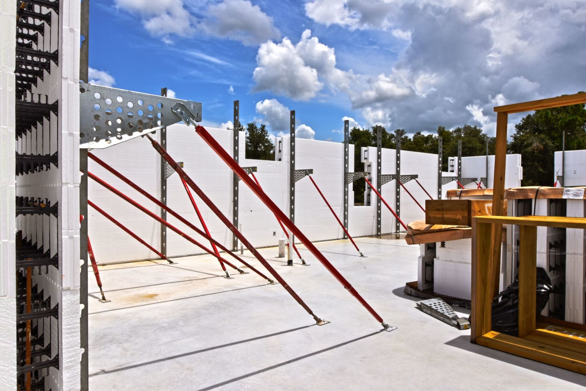 Construction site with white insulated concrete forms, red bracing, and a blue sky.