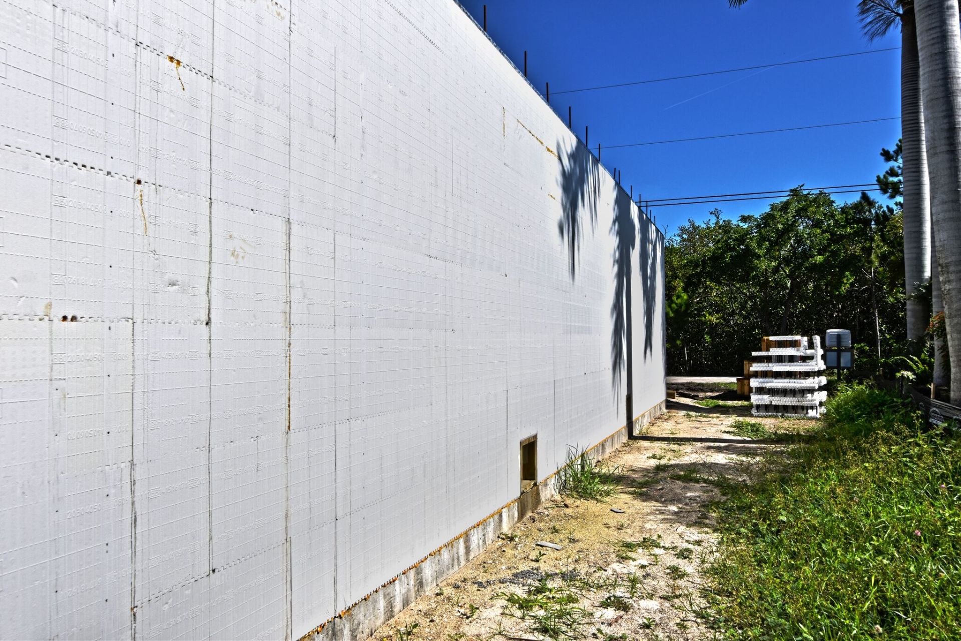White building with a side path, under a blue sky, with some grass and trees on the right.