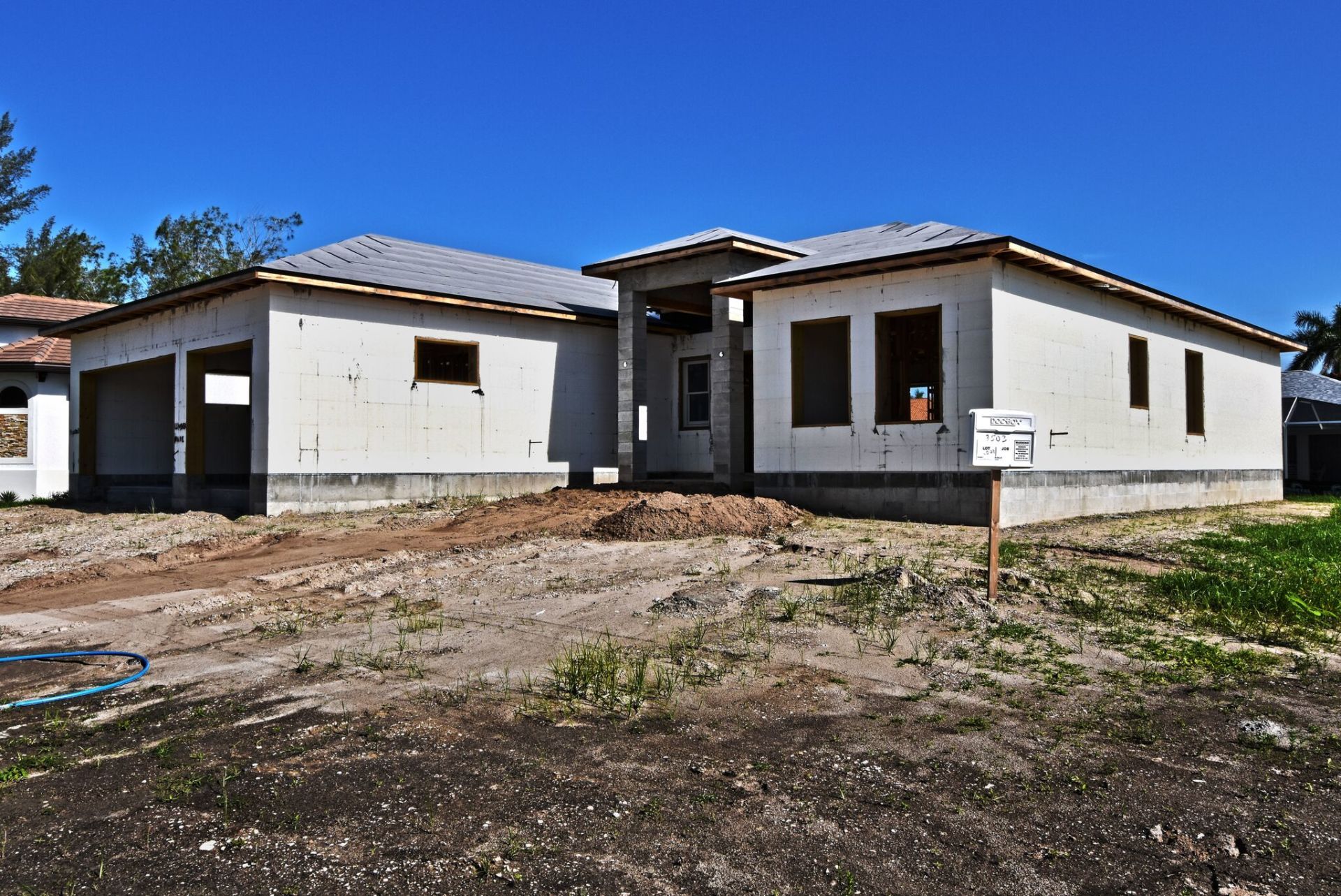 House under construction; exterior walls built, roof framing, blue sky.