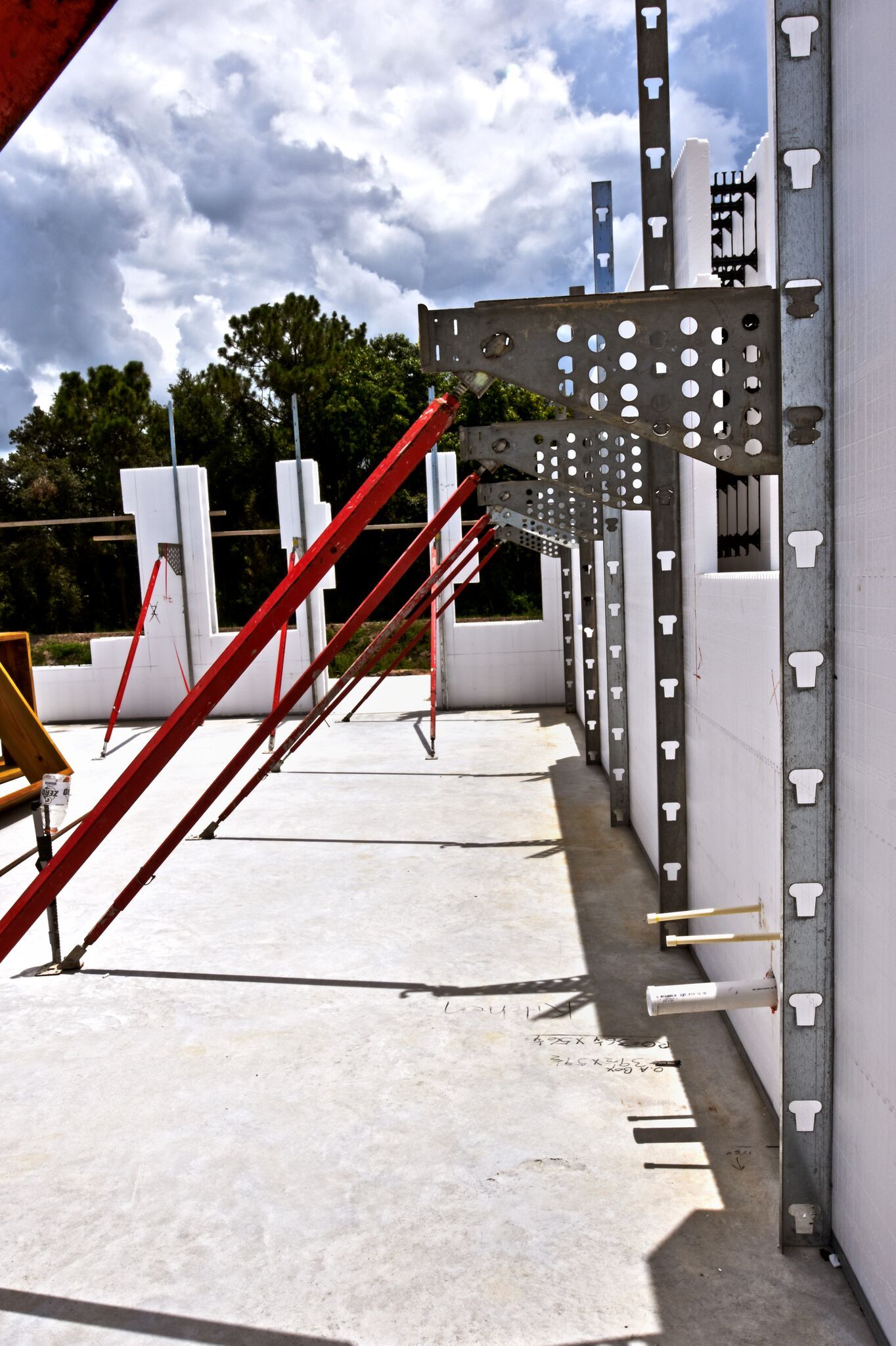 Construction site: white insulated concrete forms with metal supports; red braces; concrete floor; blue sky.