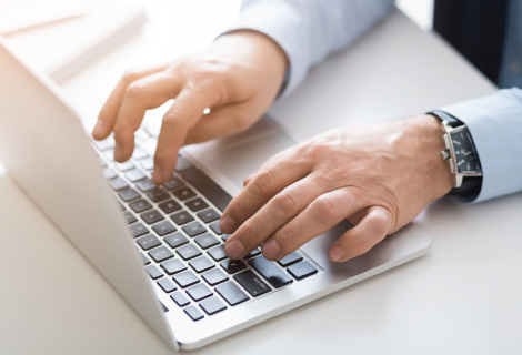 Hands typing on a laptop, close-up, indoors. Watch visible on one wrist.