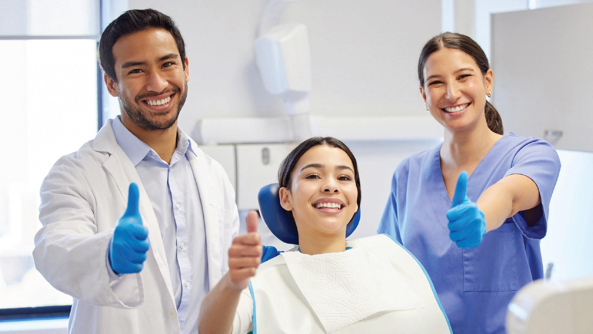 Dentist, patient, and assistant giving thumbs up in a dental office.
