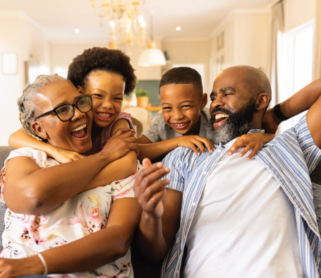 Family smiling and laughing, embracing on a couch in a living room.