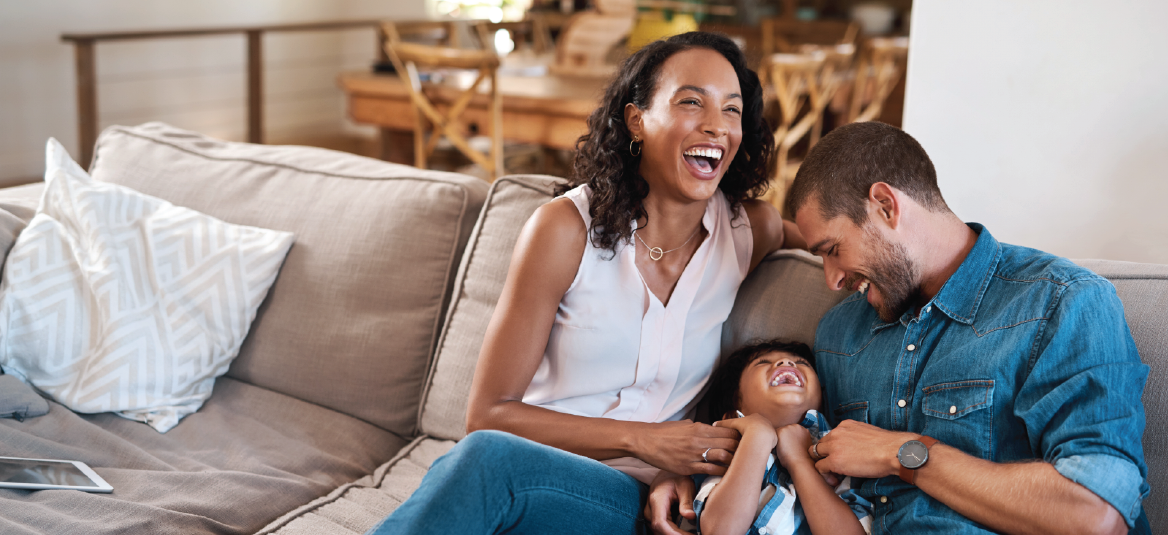 Family laughing together on a couch in a living room, enjoying each other's company.