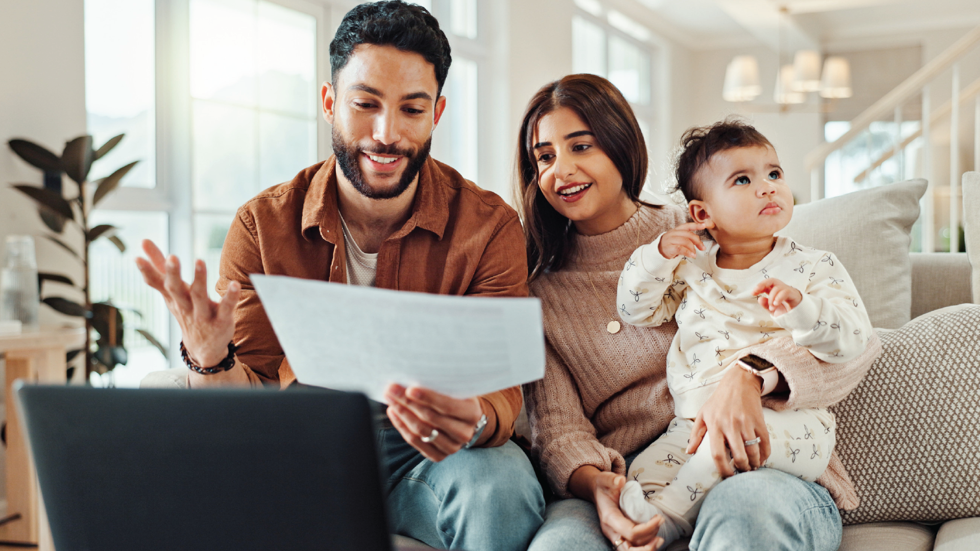 Family looking at papers together while seated on a couch; laptop is open.