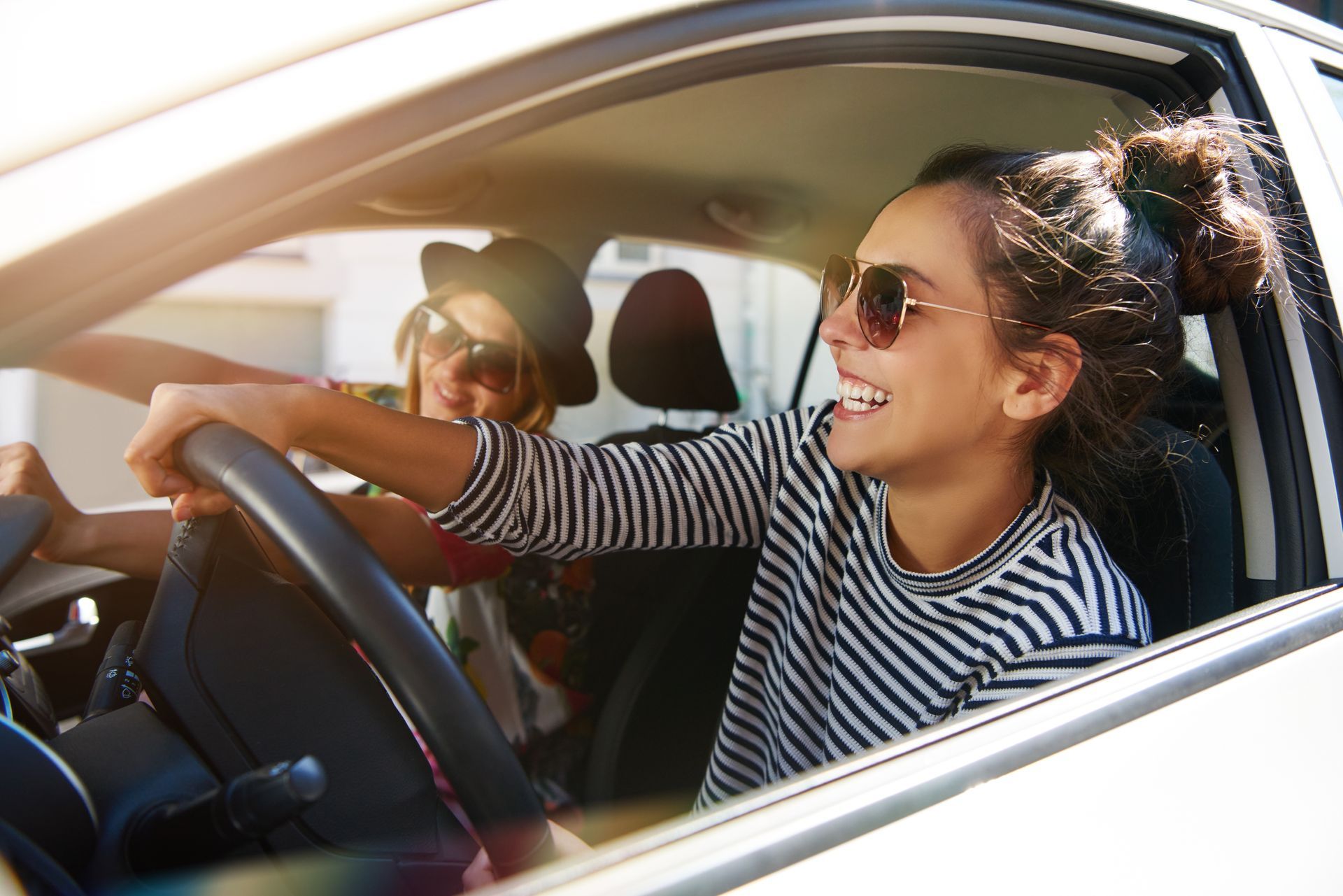 Two laughing young girlfriends driving together in a car