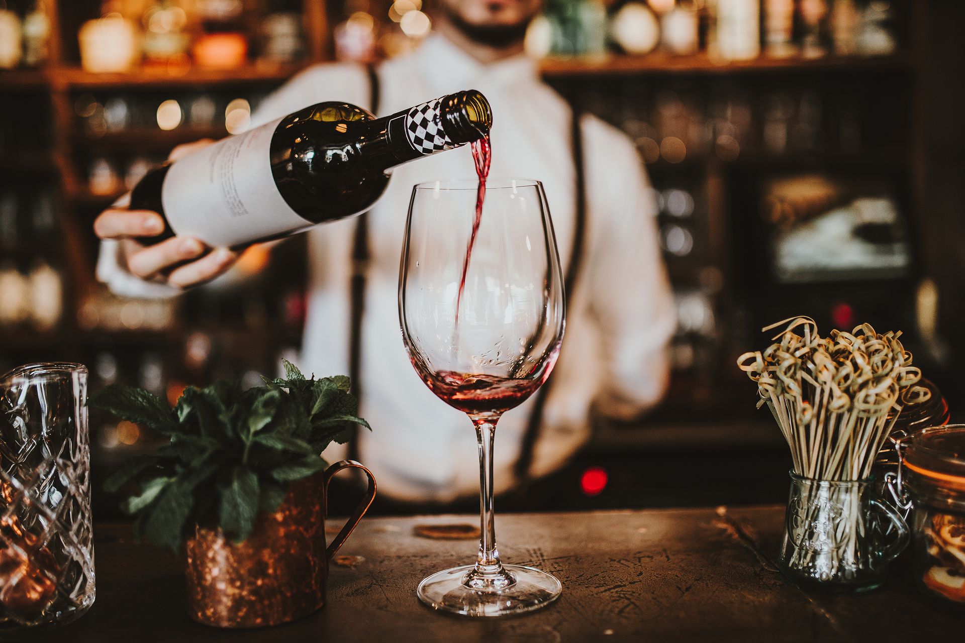 Close up shot of a bartender pouring red wine into a glass. Hospitality, beverage and wine concept.