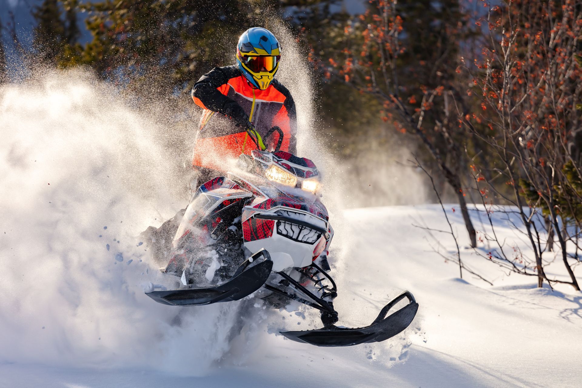 the guy is flying and jumping on a snowmobile on a background of winter forest  leaving a trail of splashes of white snow. bright snowmobile and suit without brands. extra high quality