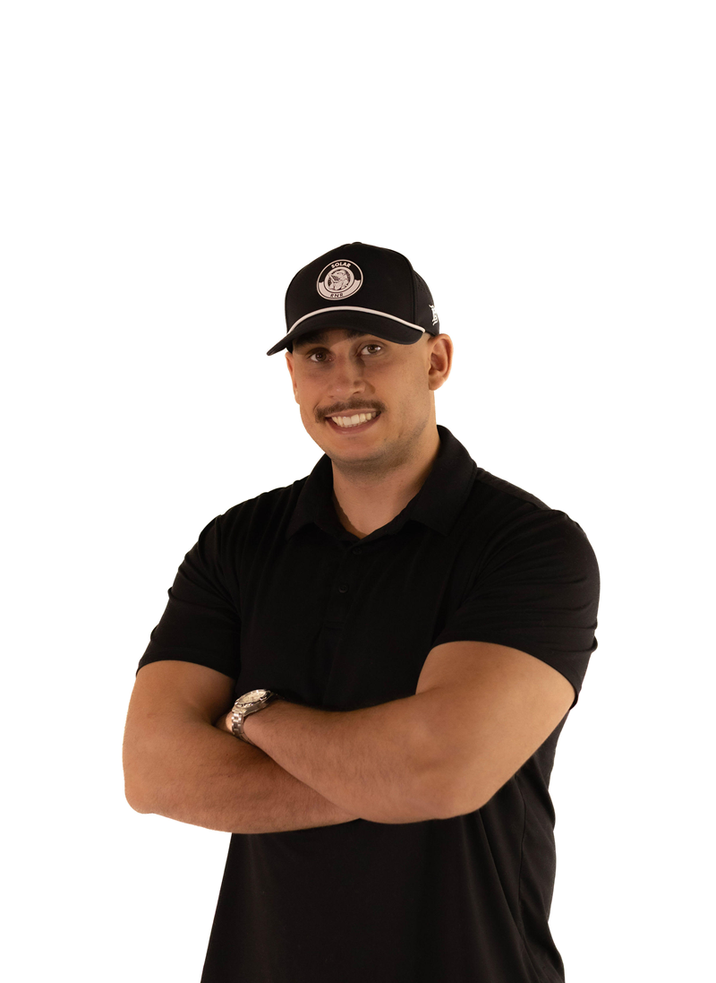 Man with arms crossed, wearing black cap and polo shirt, smiling.