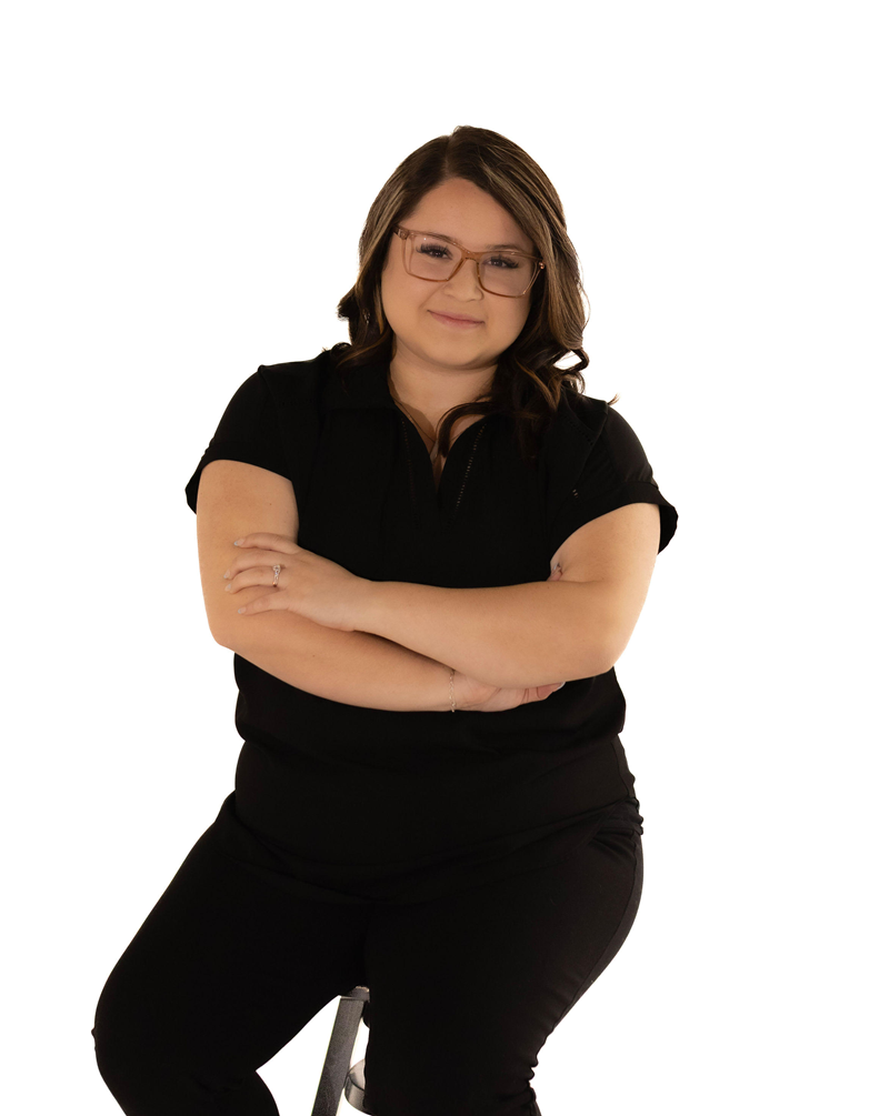 Woman with glasses, arms crossed, wearing black sitting on a stool.