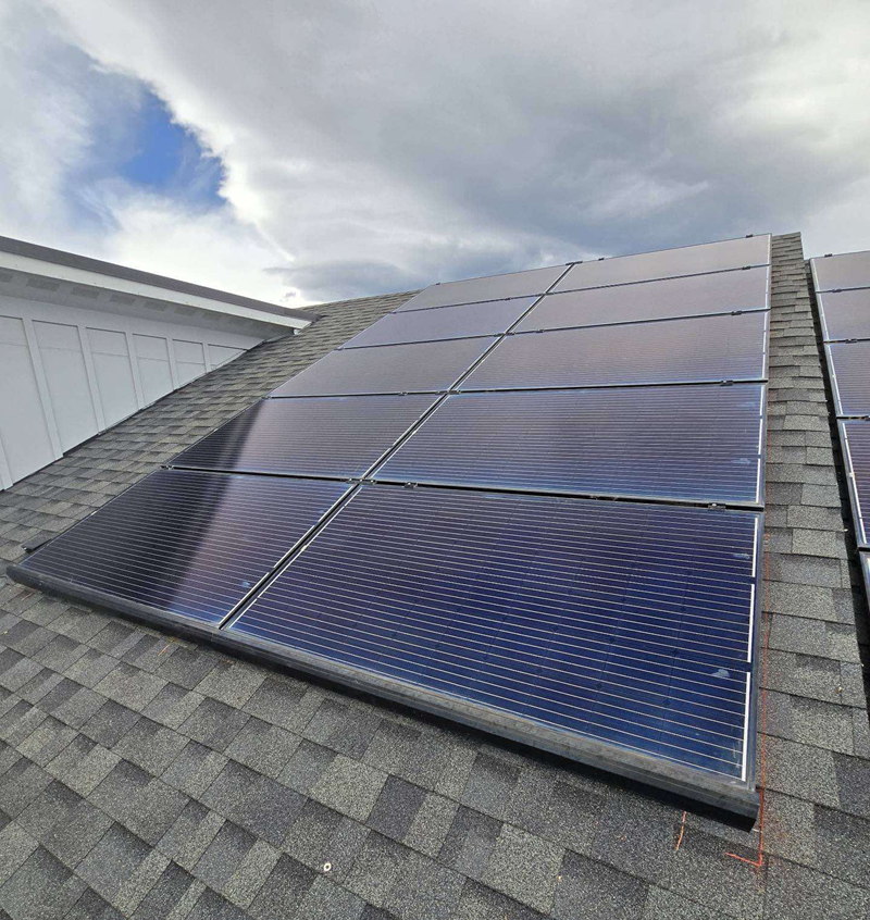 Solar panels installed on a gray shingle roof under a cloudy sky.