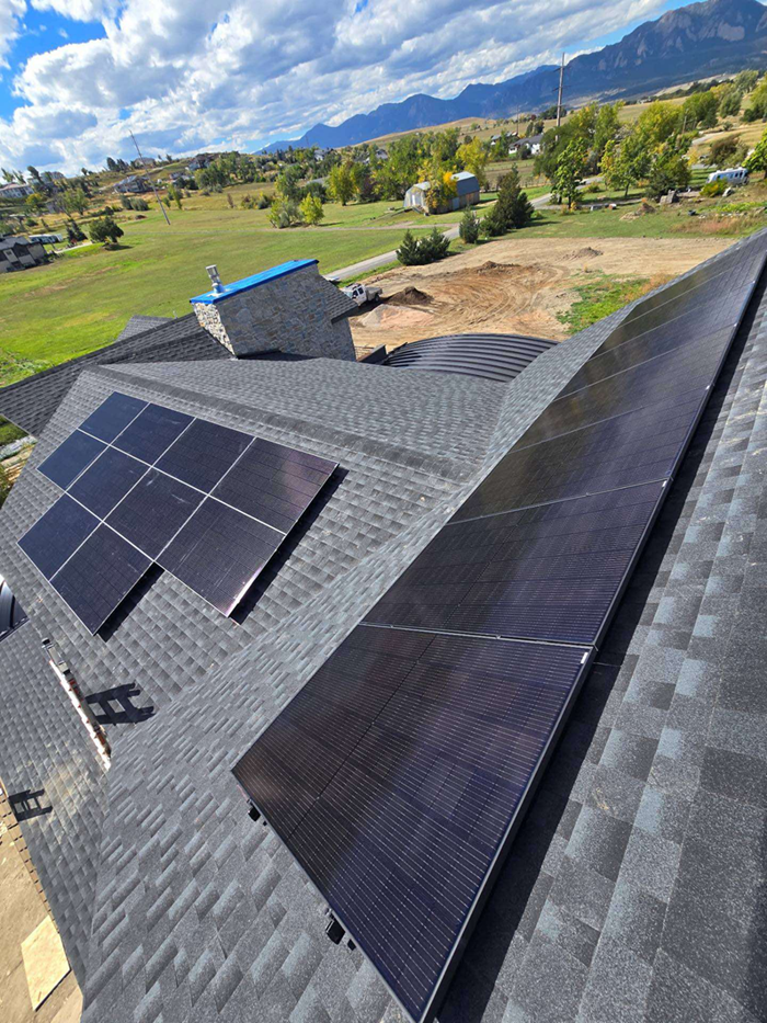 Solar panels on a dark shingled roof, with mountain and sky background.