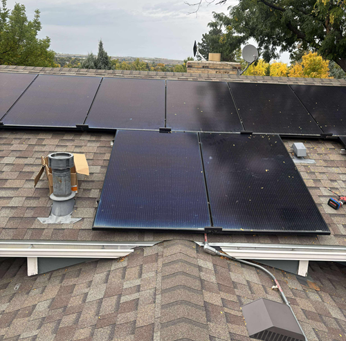Solar panels installed on a brown shingled roof, overcast sky.