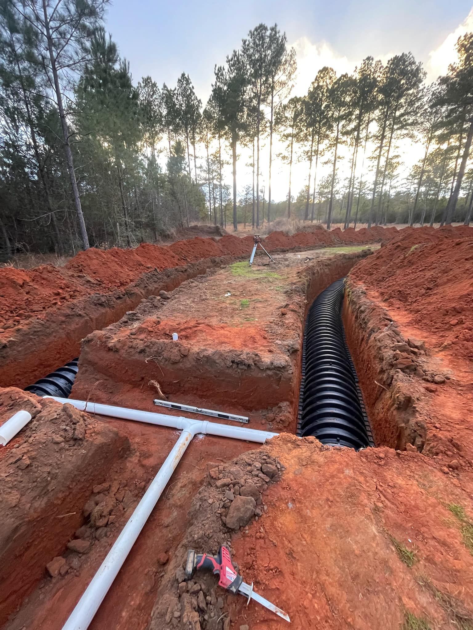 Heavy Duty Pumping | A drainage system is being installed in a dirt field with trees in the background.
