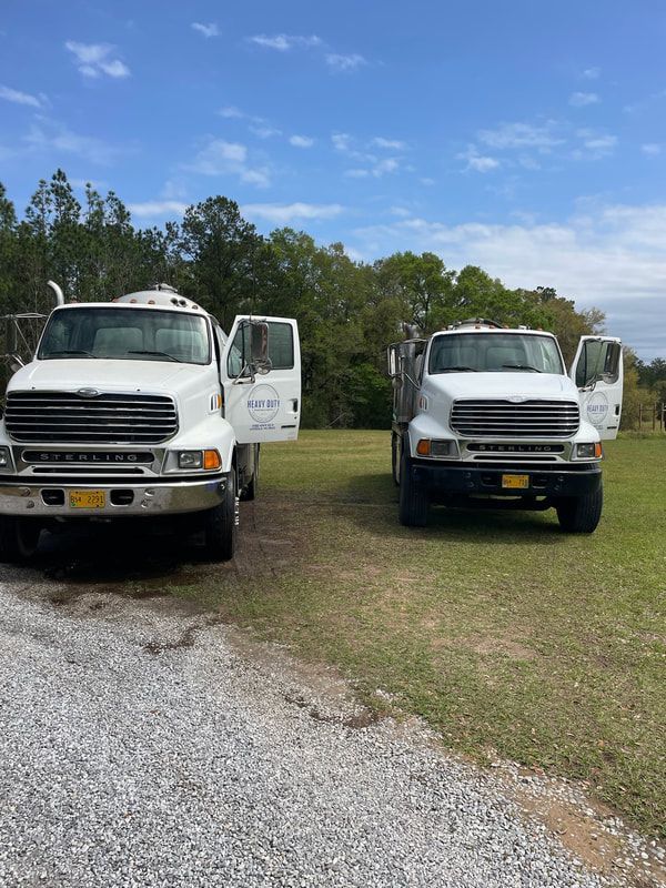Heavy Duty Pumping | Two white trucks are parked next to each other on a gravel road.
