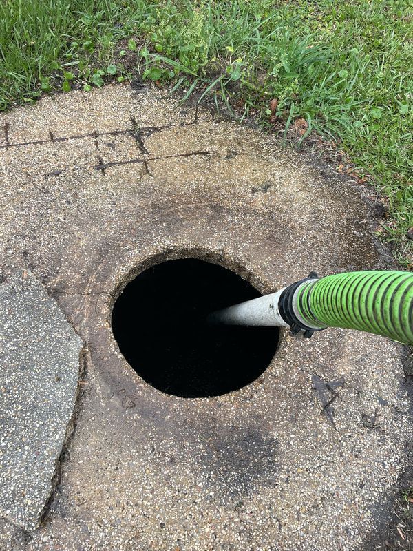 Heavy Duty Pumping | A person is pumping water into a septic tank with a green hose.