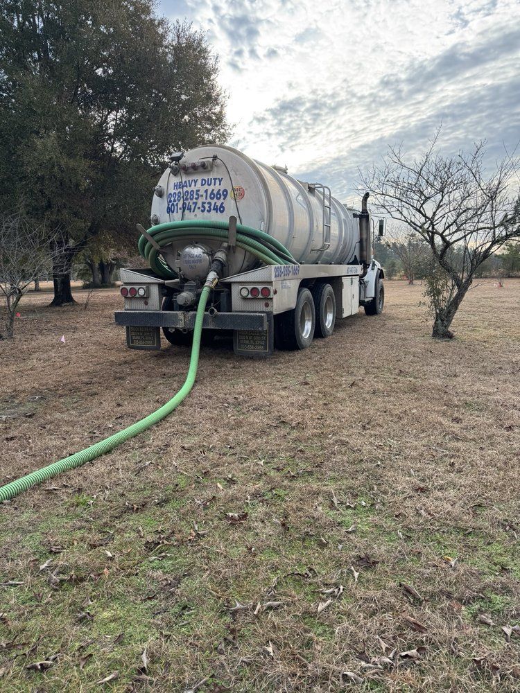 Heavy Duty Pumping | A septic truck with a green hose attached to it is parked in a field.