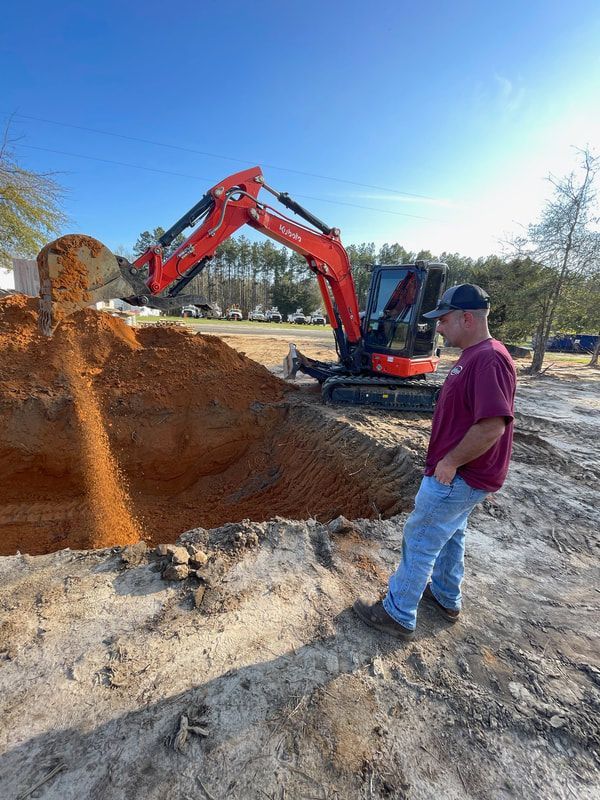 Heavy Duty Pumping | A man is standing in front of a large pile of dirt next to an excavator.