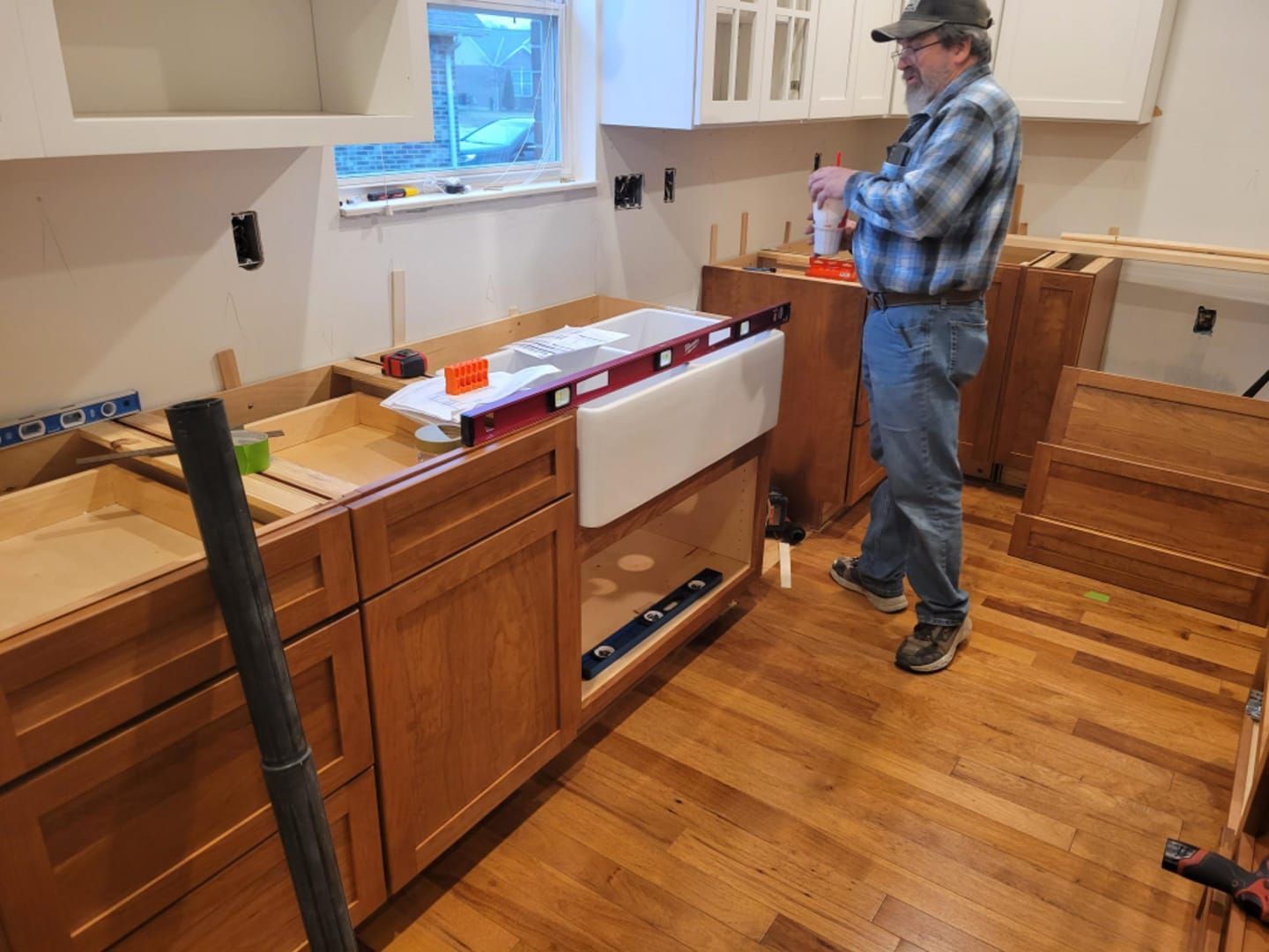 Man installing a kitchen sink, with cabinets, level, and other construction tools in a room with wood floors.