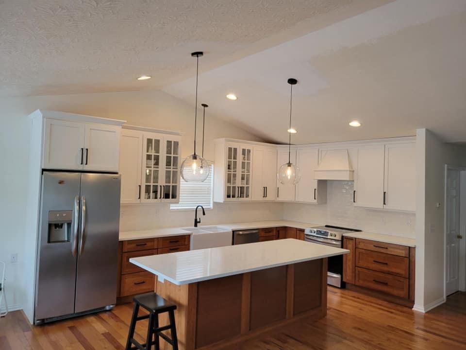 A renovated kitchen with white and wood cabinets, stainless steel appliances, and a center island with pendant lights.