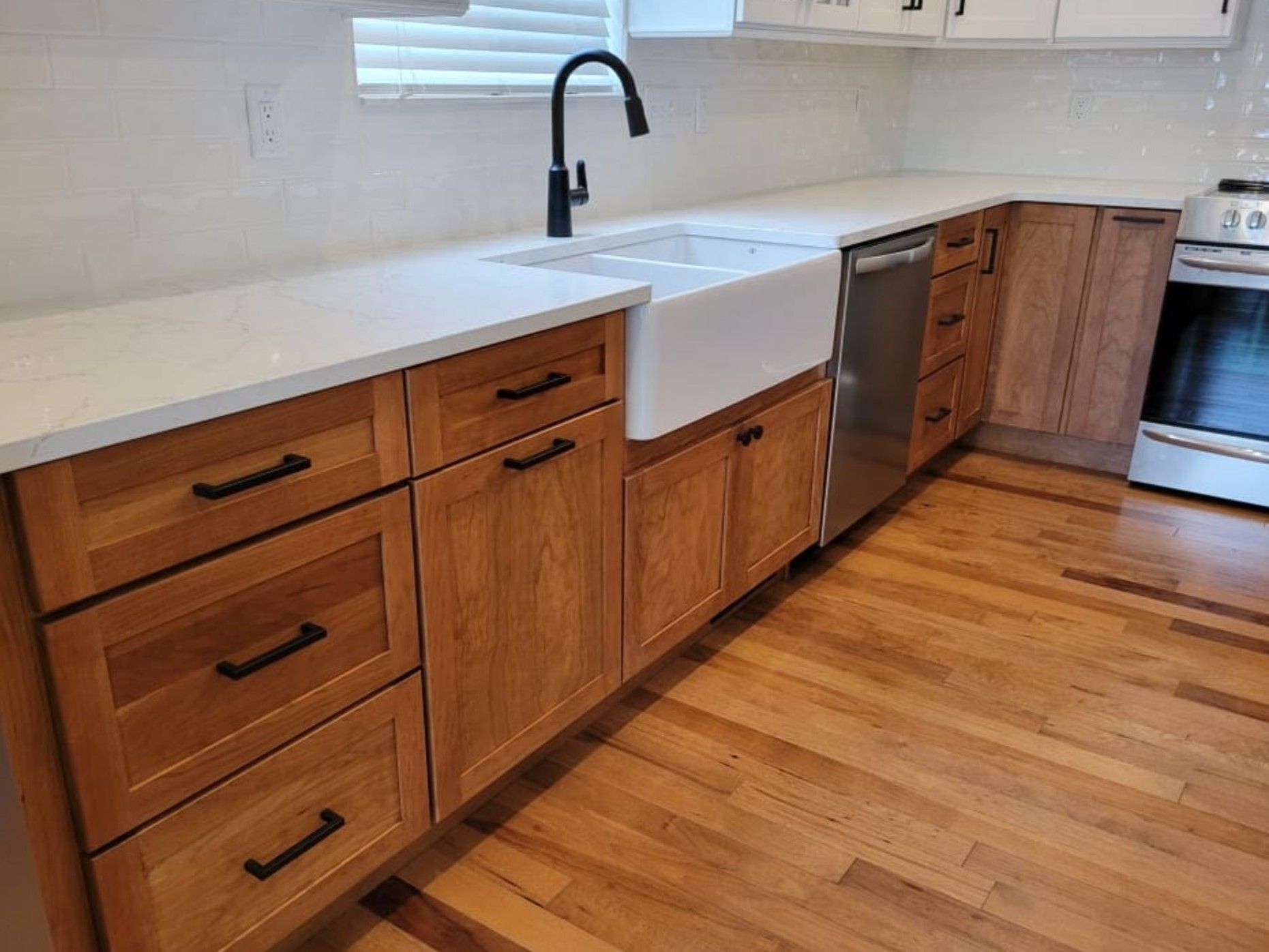 Kitchen with light wood cabinets, white countertop, farmhouse sink, and black faucet.