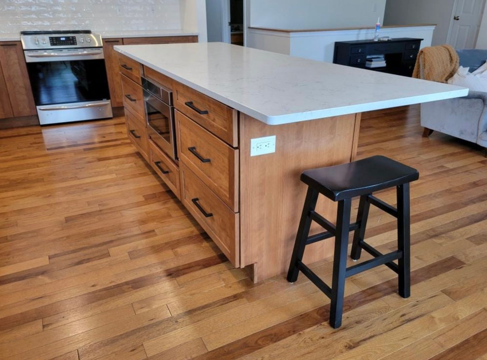 Kitchen island with light-colored countertops and cabinets, with a black stool in front.
