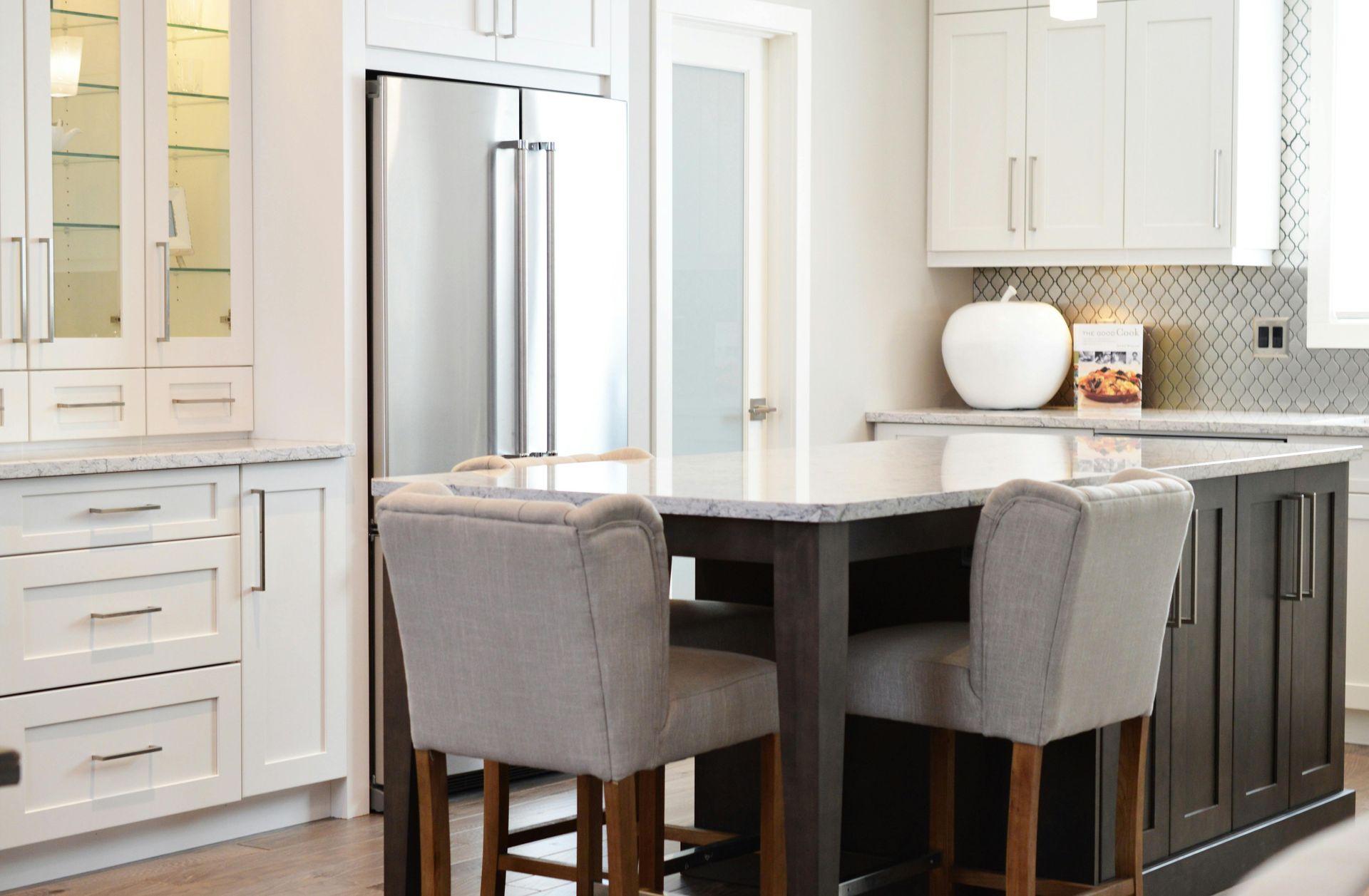 Modern kitchen with a dark island, light cabinets, and gray barstools. Stainless steel fridge.